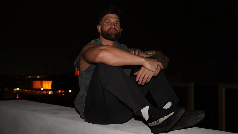 Caleb Hellinger seated on a rooftop ledge at night